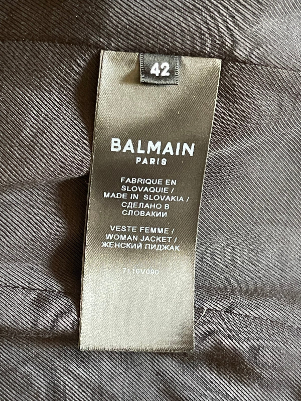 A close-up of a Balmain Paris size 42 garment tag sewn onto black  textured fabric.
