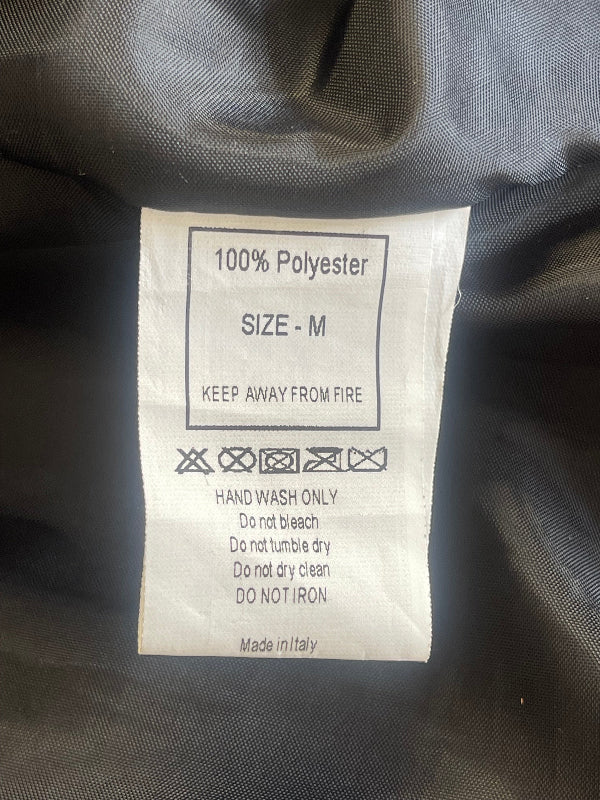 A close-up of a white polyester care label inside a dark gray garment, showing size M and care instructions including hand wash only and do not iron.