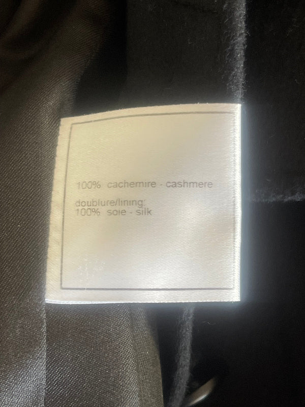 A close-up of a white fabric care label sewn onto a dark black garment, showing text that reads '100% cachemire - cashmere' and 'doubleure/lining: 100% soie - silk'.