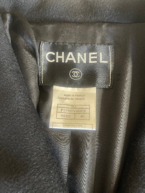 Close-up of a Chanel garment interior showing the black satin neck label with white CHANEL text and logo, plus a smaller white size/information tag below it.
