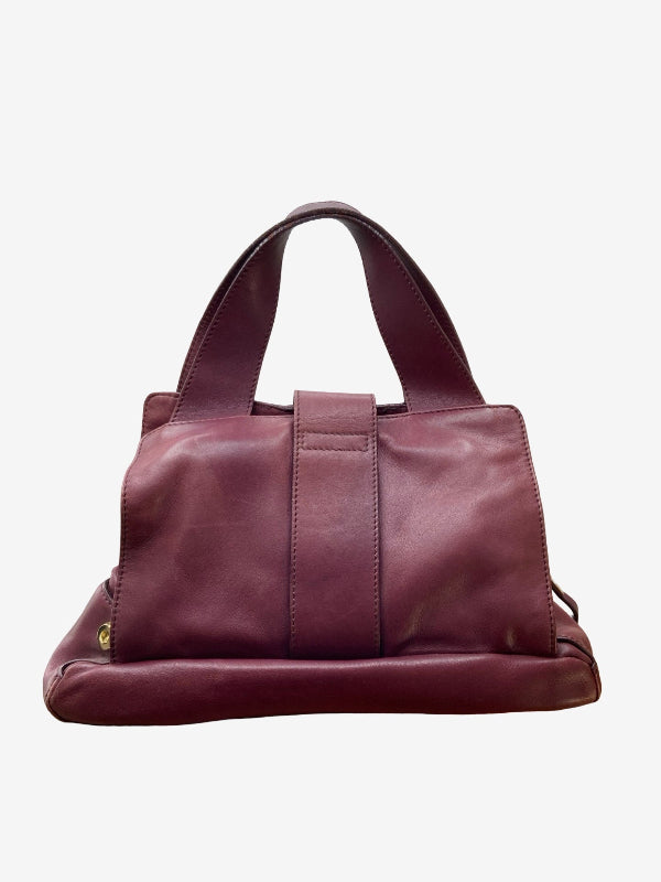 A burgundy leather handbag with dual top handles and a front strap closure, shown against a plain light gray background.