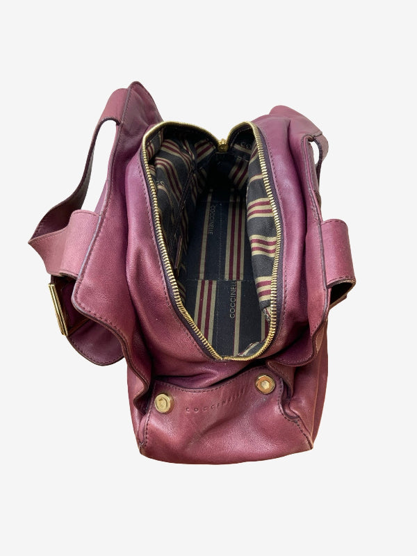 A dusty rose leather shoulder bag shown open, displaying its striped interior lining and gold-tone hardware, set against a plain light gray background.