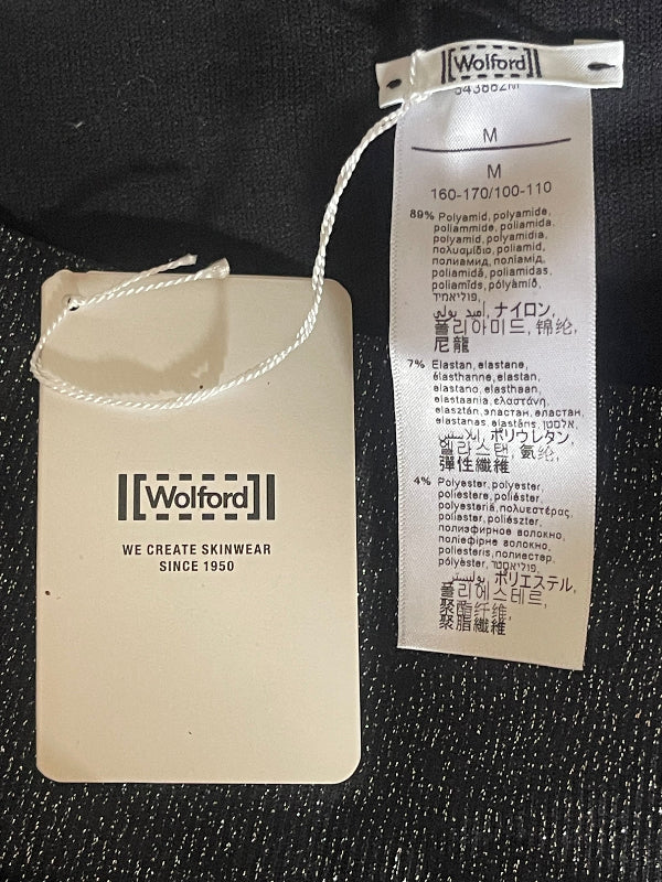 A close-up of a garment tag and size label sewn onto black textured fabric. The paper tag is cream-colored with the brand name 'Wafred' and the text 'WE CREATE SKINWEAR SINCE 1960'.