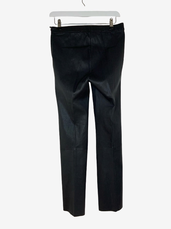Black leather pants hanging on a white hanger against a light gray background.