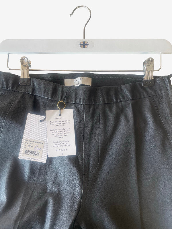 Black lambskin  leather trousers hanging on a white hanger with price and brand tags visible.