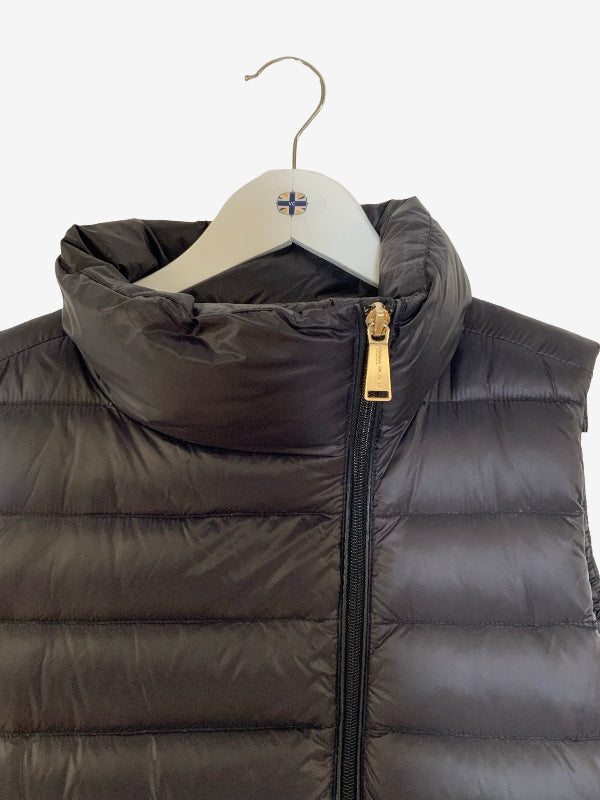 A black puffer vest with a high collar and gold zipper pull, hanging on a white hanger with a small cross logo.