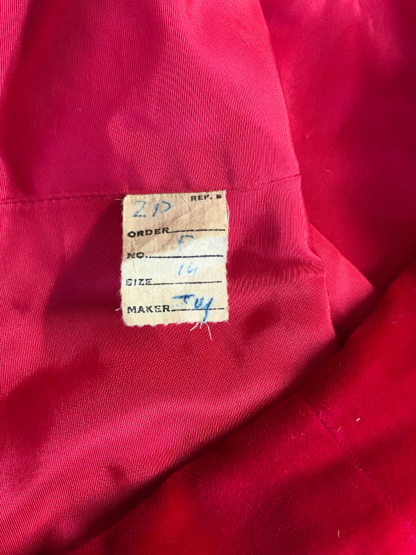 A close-up of a bright pink or magenta satin-like garment interior with a small sewn paper size label reading 210, order P, no. 14, size 14, maker Tu.