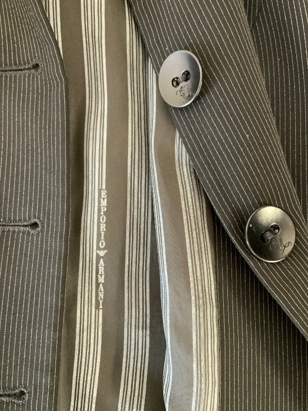 Close-up of a striped suit jacket and striped lining with black buttons. The lining displays the vertical text 'EMPORIO ARMANI' on the inner placket.