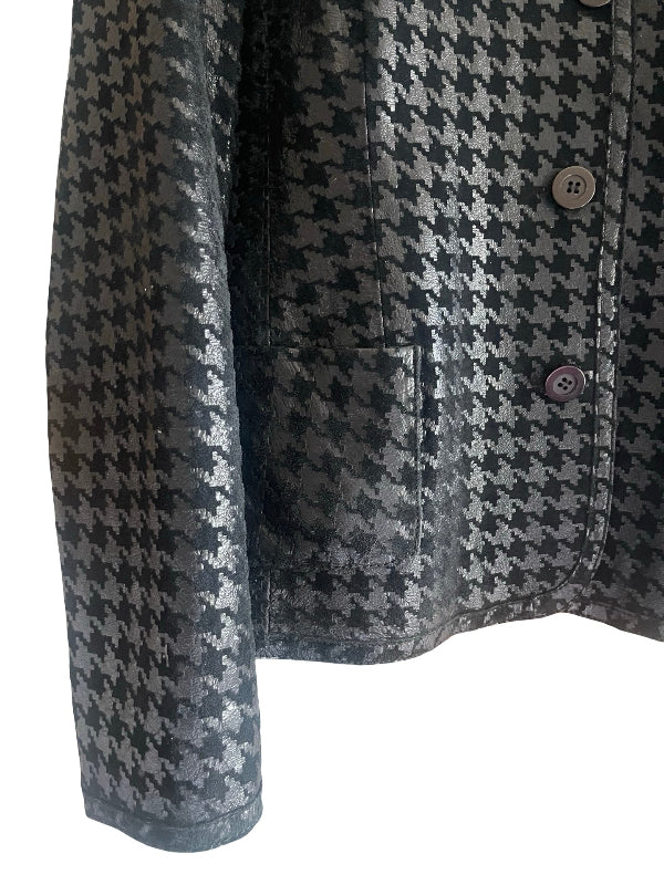 Close-up of a black and black tone houndstooth patterned jacket with a button closure and a pocket, shown against a plain white background.