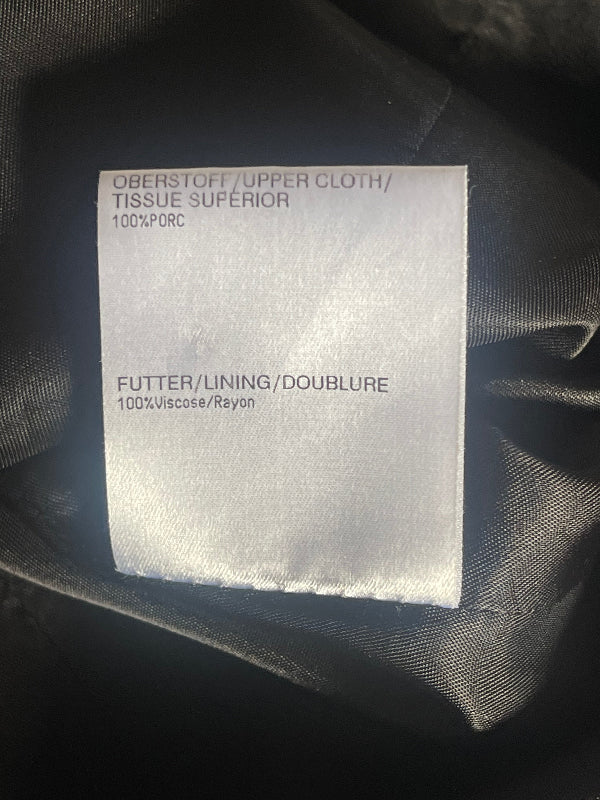 A close-up of a white satin fabric label sewn onto dark black fabric, showing printed text in German and French.