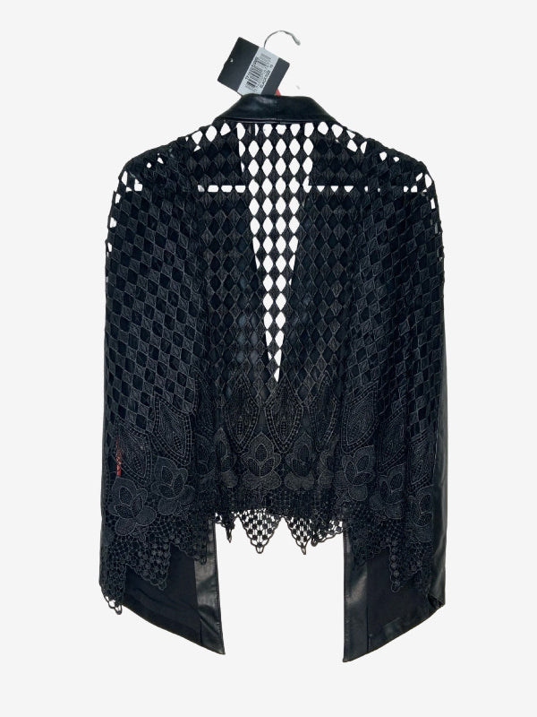 A black open-knit lace cape with floral embroidery and sheer mesh panels, hanging on a black hanger against a light gray background.