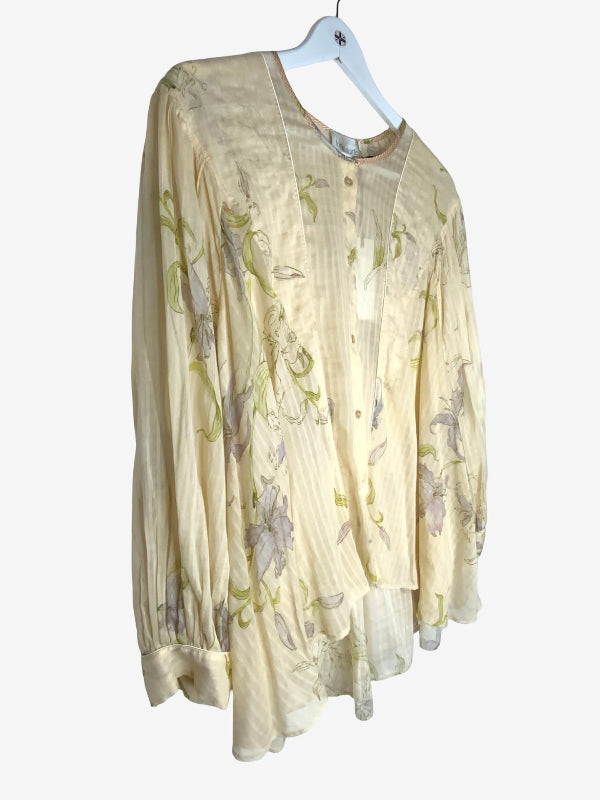 A long-sleeve blouse in a light cream or pale yellow fabric with a subtle green and lavender floral print, hanging on a white hanger against a plain light gray background.