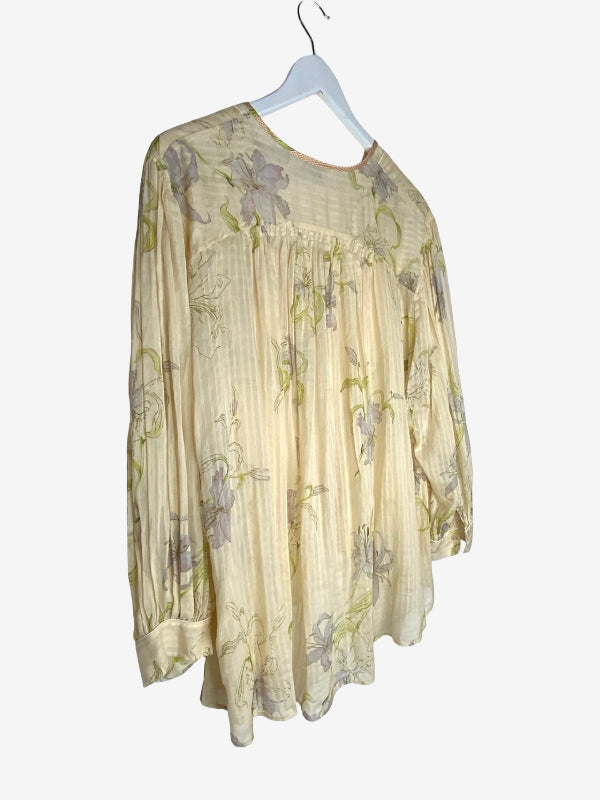 A cream-colored long-sleeve blouse with a subtle floral print in muted purple and green, hanging on a white hanger against a light gray background.