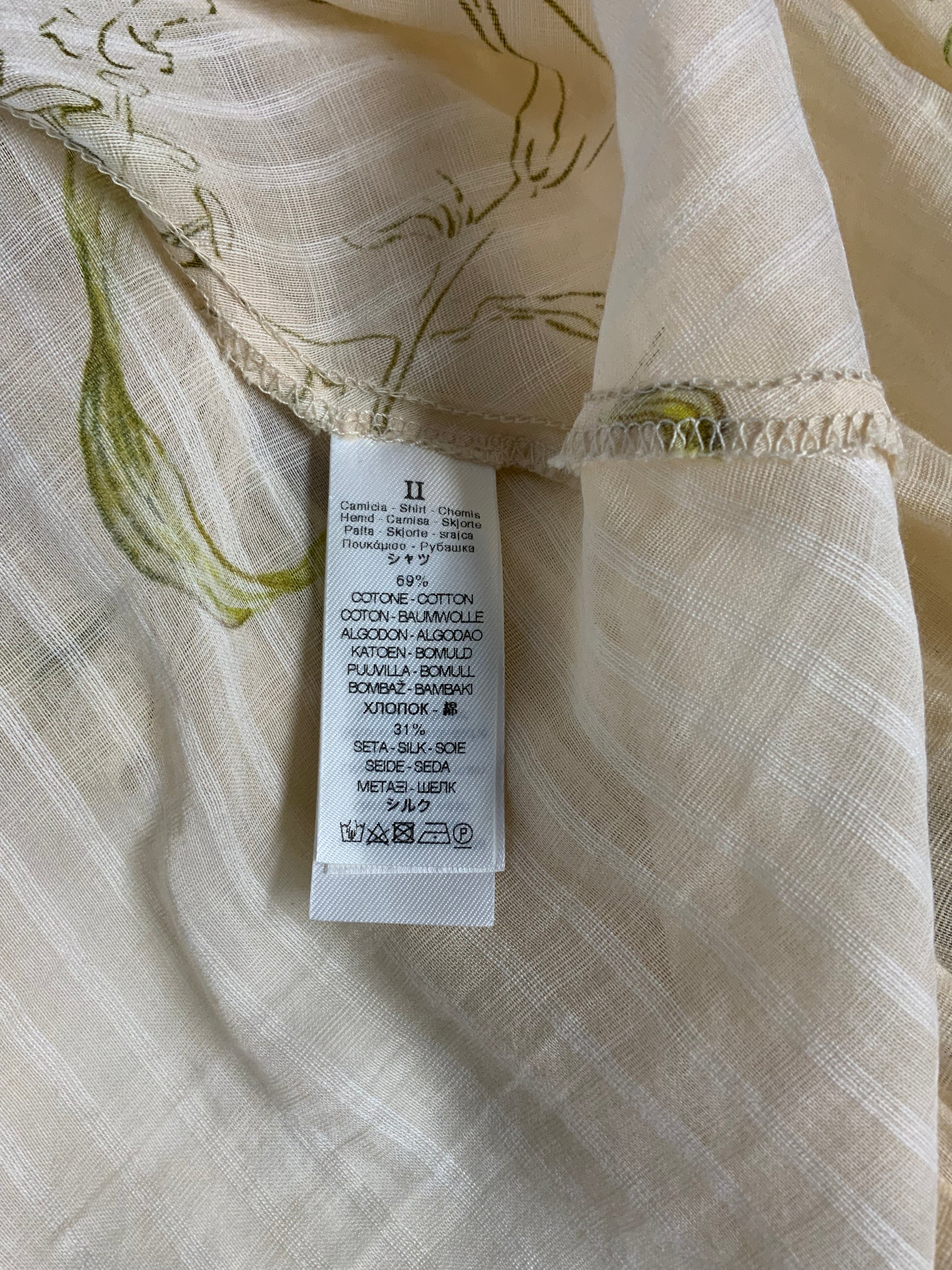Close-up of a cream-colored cotton-blend garment with a green botanical pattern and a white sewn-in size tag showing fabric composition.