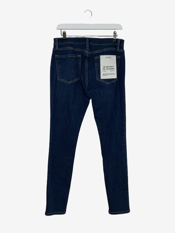 Dark blue denim jeans shown from the back, hanging on a white plastic hanger against a light gray background. A white paper label is visible on the back pocket.