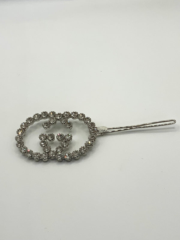 A silver-tone hair claw clip embellished with a double-G style interlocking monogram design and surrounded by clear rhinestones, shown on a plain white background.