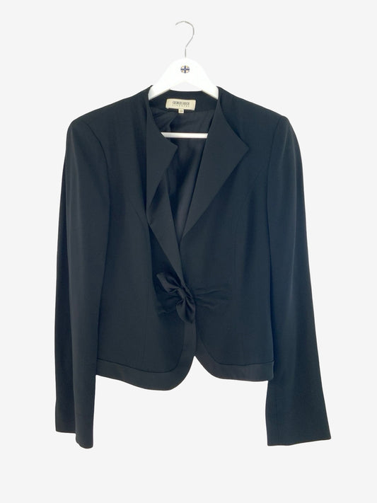 A black cropped blazer with a unique front twist detail, hanging on a white hanger against a light gray background.