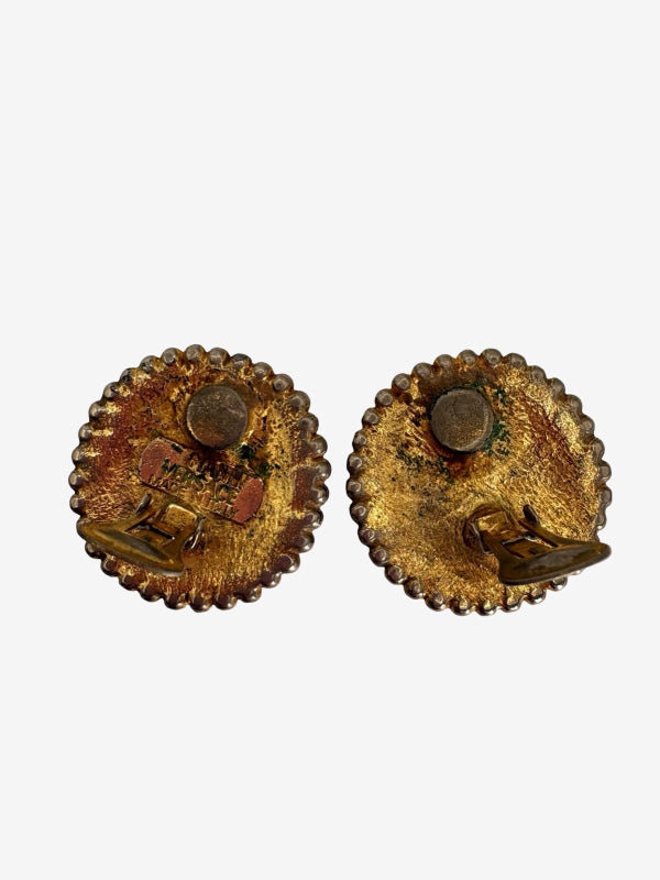A pair of vintage gold-toned oval earrings with scalloped edges, featuring a central round stone and a small dangling gold charm, shown against a plain light gray background.