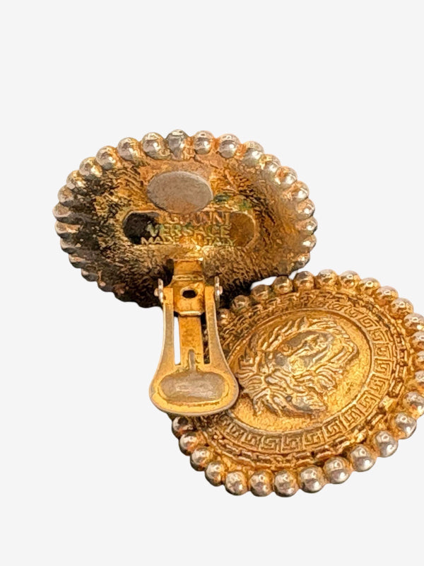 A gold-tone oval pin with a raised lion head motif and a beaded border, shown with its clasp mechanism open against a plain light background.