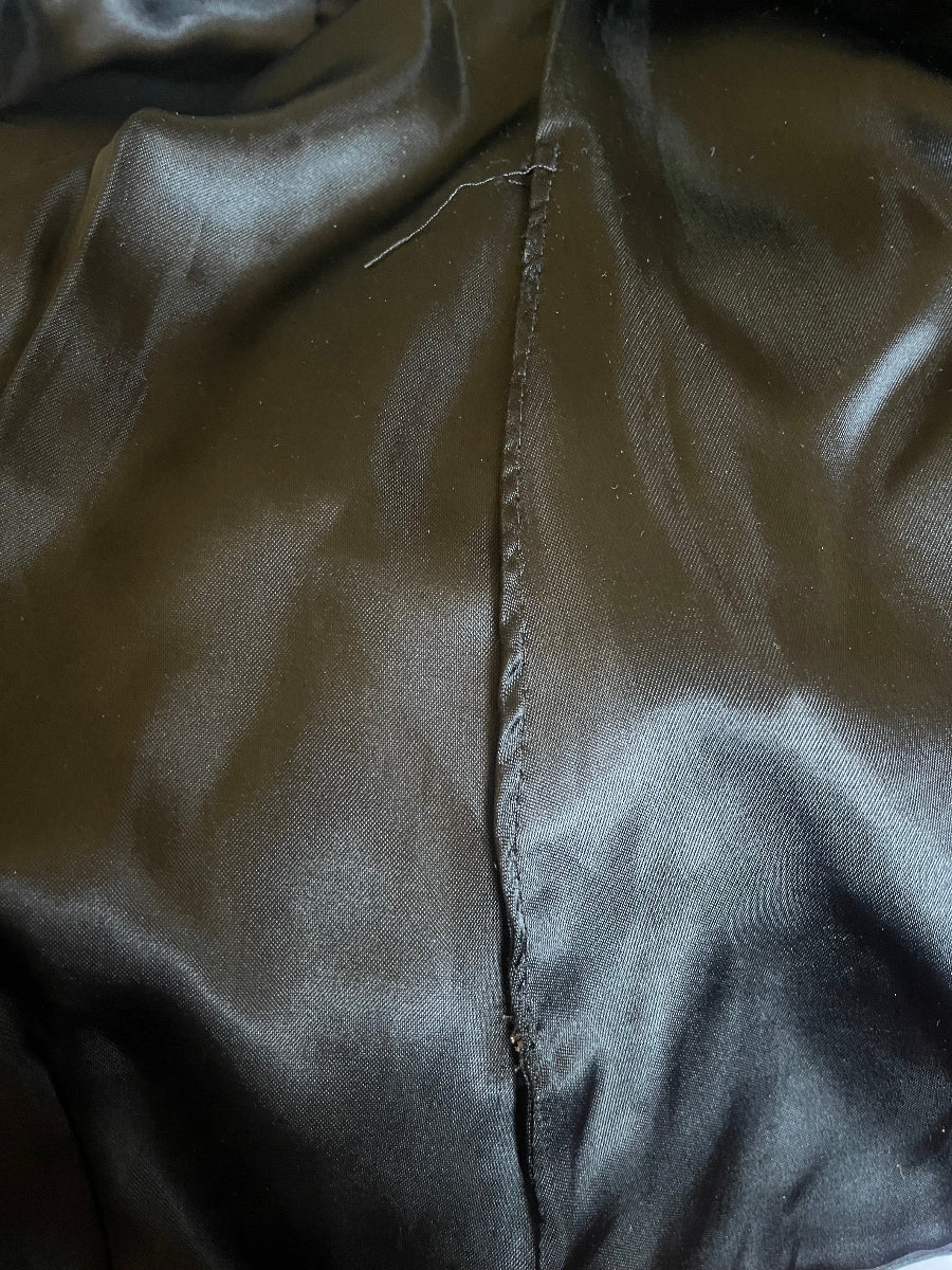 Close-up of a dark black satin or silk-like fabric lining with a horizontal stitched  repair seam.