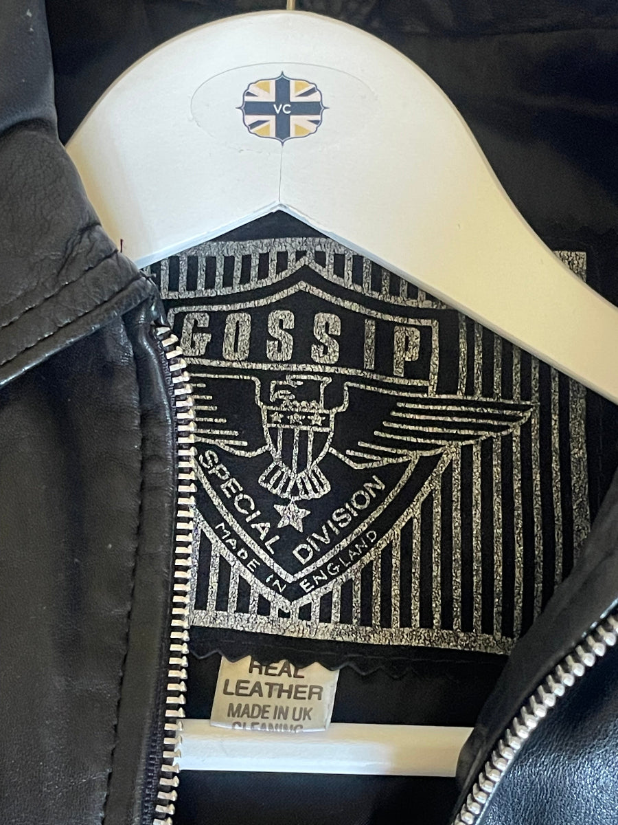 Close-up of a black leather jacket interior showing a black-and-white embroidered 'FSSP Special Division' patch, a white plastic hanger with a cross emblem, and a sewn label reading 'Real Leather Made in Vietnam'.