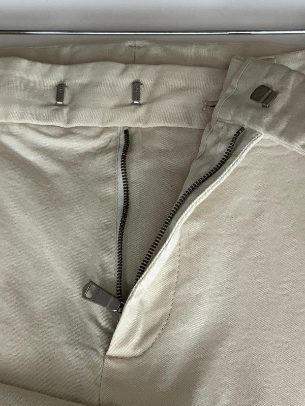 Close-up of a light beige or cream-colored garment, showing a zipper closure, metal zipper pulls, and fabric texture.