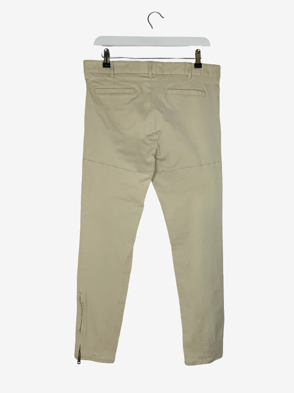A pair of light beige slim-fit trousers shown from the back, hanging from a white hanger with black clips against a plain white background.