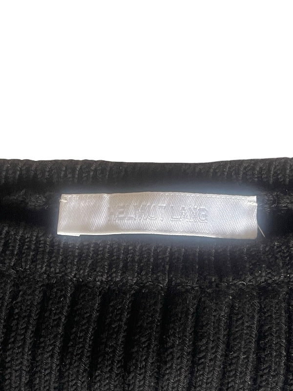 Close-up of a black ribbed knit garment showing a white fabric brand label that reads 'HELMUT LANG'.