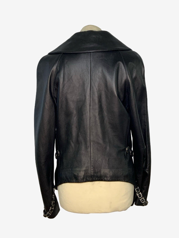 A black leather jacket with a wide collar and chain-link details on the cuffs, displayed on a cream-colored mannequin torso against a light gray background.