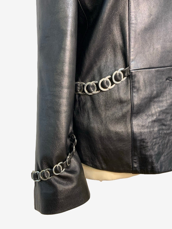 Close-up of a black leather jacket featuring a decorative silver-tone metal ring chain detail running along the side seam and cuff.