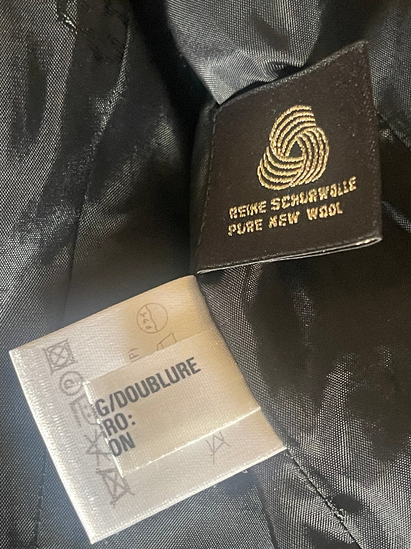 Close-up of a black garment interior showing a dark brown woven label with gold text reading 'REINE SCHWARZWILLE PURE BLACK WOOL' and a white size/care tag.