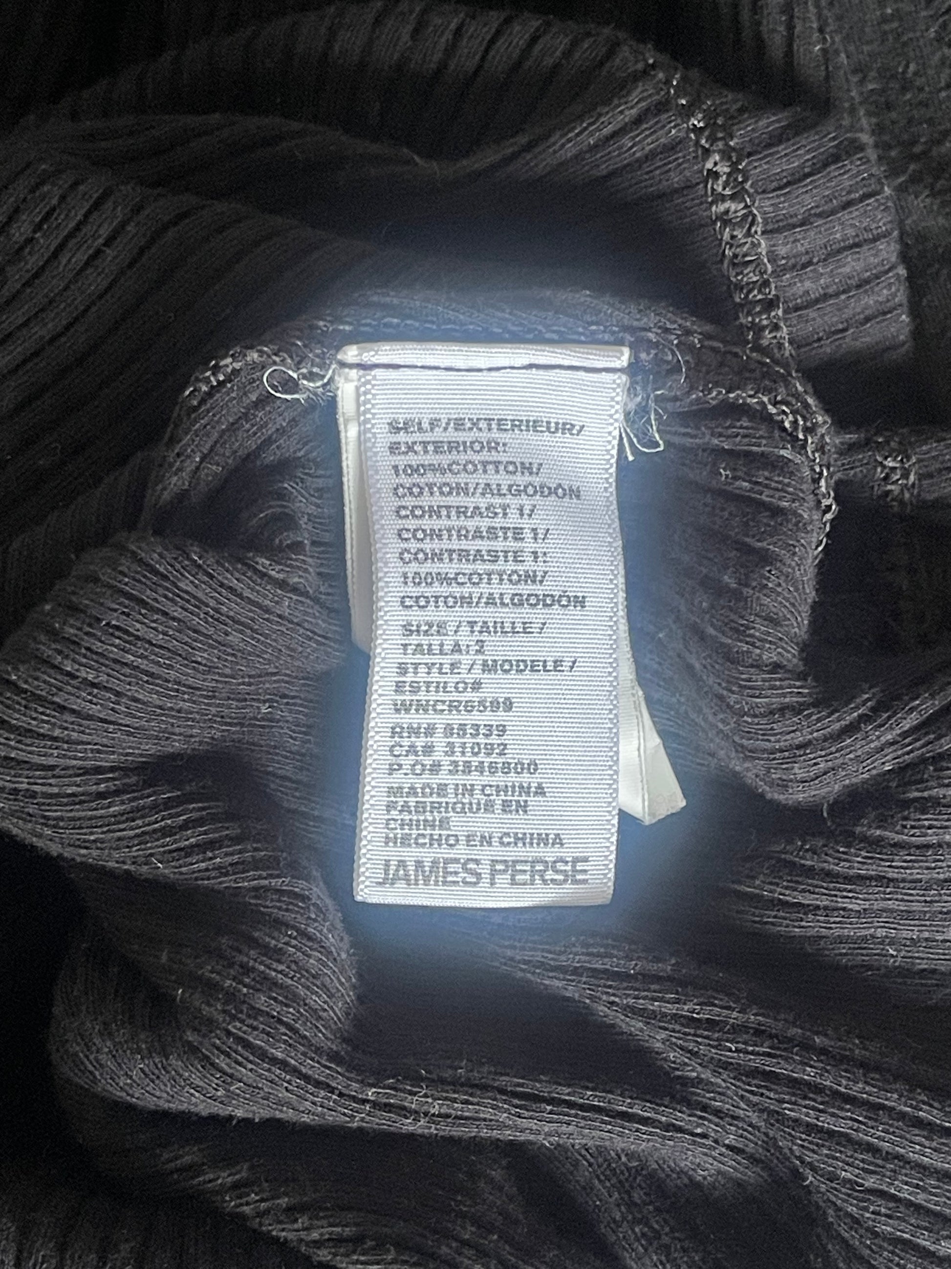 Close-up of a black ribbed knit garment with a visible sewn-in label reading JAMES PERSE.