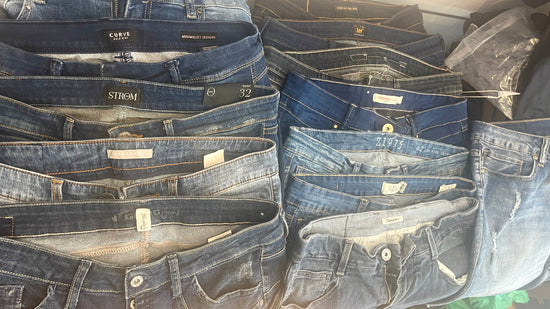 A close-up arrangement of multiple pairs of folded blue denim jeans showing waistbands, labels, and front pockets, with no person or real environment visible.