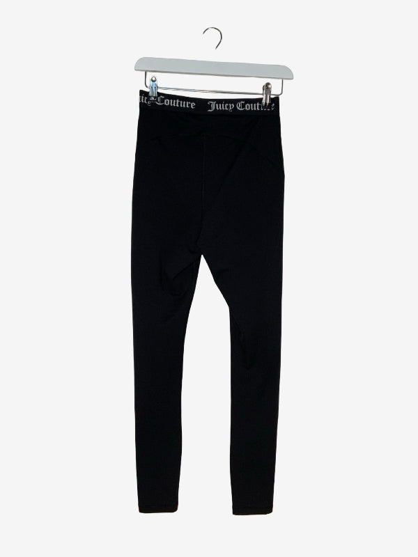 Black slim-fit leggings hanging from a white hanger, featuring a branded elastic waistband with 'Juicy Couture' text.