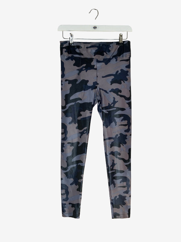 A pair of full-length leggings with a dark blue and gray camouflage pattern, hanging from a white plastic hanger against a light gray background.