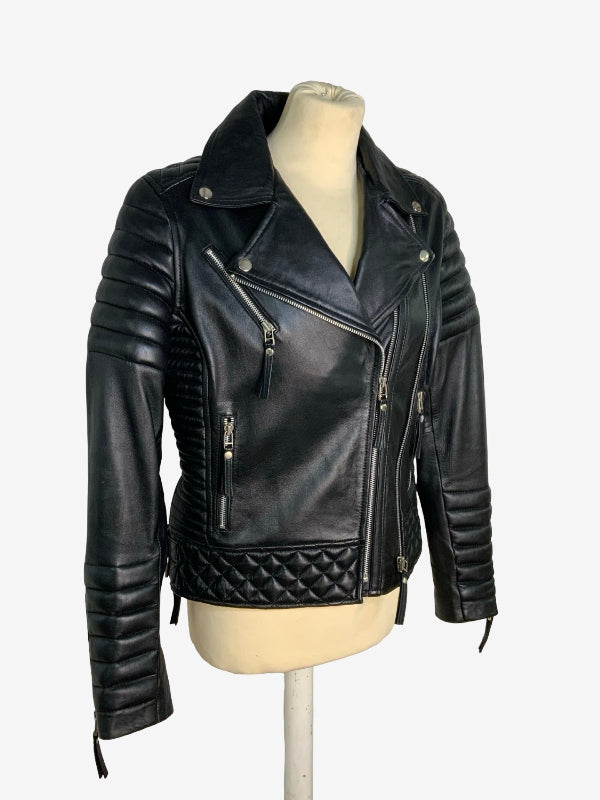 A black faux leather moto jacket with quilted and pleated details, displayed on a cream-colored mannequin torso against a plain white background.