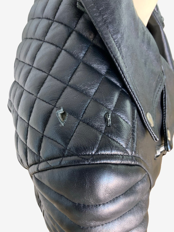 Close-up of a black quilted leather jacket on a mannequin, showing the diamond-quilted pattern, smooth leather panels, and metal snap details against a light gray background.