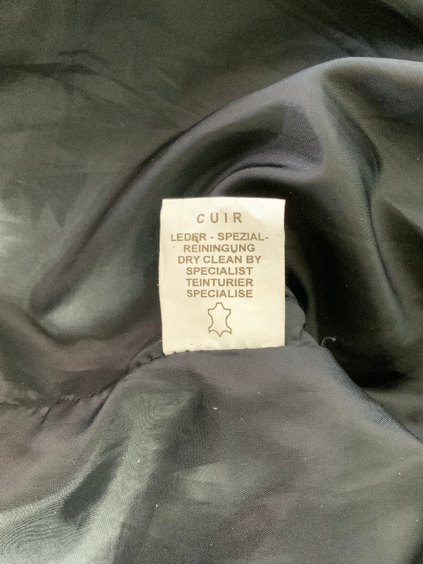 A close-up of a black quilted garment's interior label, which reads 'CUIR' and specifies leather cleaning services, set against the black fabric background.