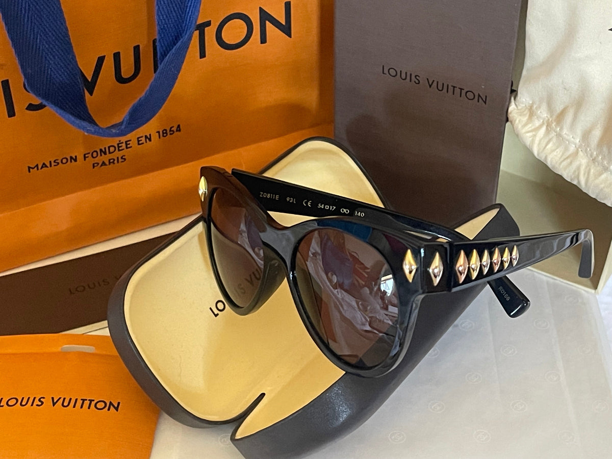 Louis Vuitton sunglasses with a black frame and gold-tone diamond accents on the temples, displayed with their signature orange and brown Louis Vuitton packaging.