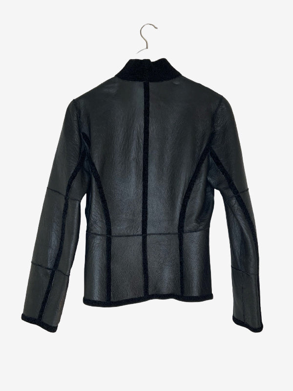 A black leather jacket with contrasting black trim and a high collar, hanging on a metal hanger against a light gray background.
