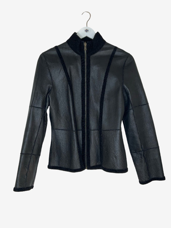 A black leather jacket with black shearling fur trim, featuring a high stand collar, zippered front, and patchwork panel details, hanging on a white hanger against a light gray background.