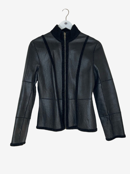 A black leather jacket with black shearling fur trim, featuring a high stand collar, zippered front, and patchwork panel details, hanging on a white hanger against a light gray background.