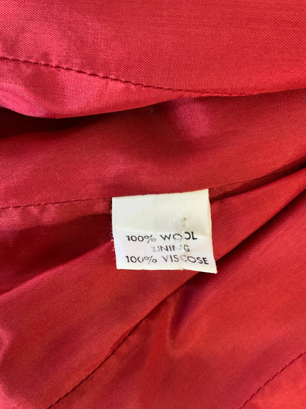 Close-up of a red garment lining with a sewn-on fabric tag reading '100% WOOL LINING 100% VISCOS'.