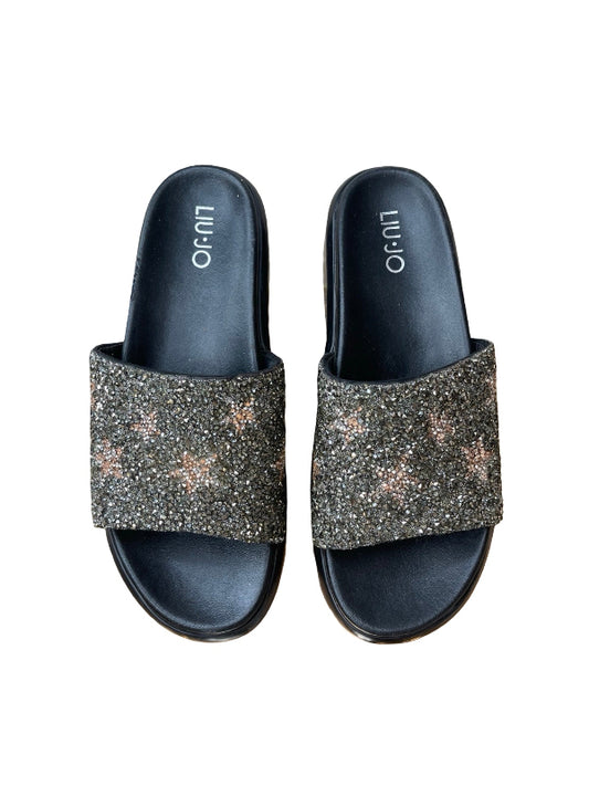 A pair of black slide sandals with glittery metallic rose gold star embellishments on the straps, shown from a top-down view on a white background. The brand name 'LUIO' is printed on the insoles.
