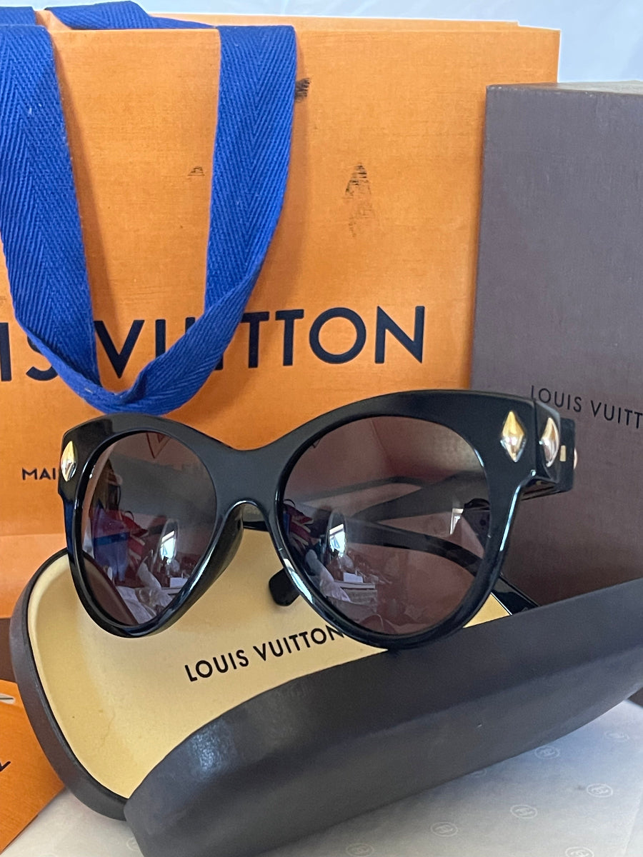 Louis Vuitton sunglasses with black frames and dark lenses, displayed on top of an orange Louis Vuitton box with a blue ribbon, alongside the gray Louis Vuitton case.