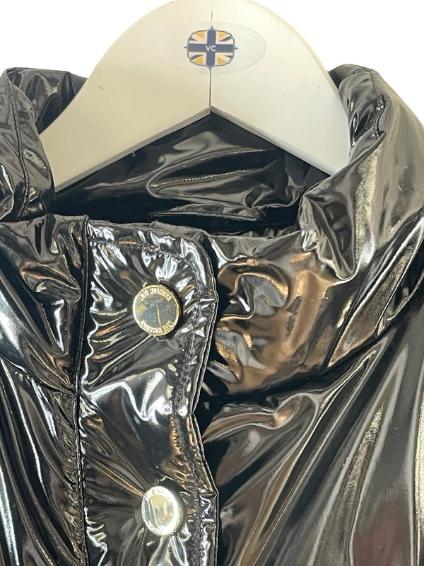 A close-up of a shiny black puffer jacket on a white hanger, showing the glossy fabric texture, a snap-button closure, and the hanger label.