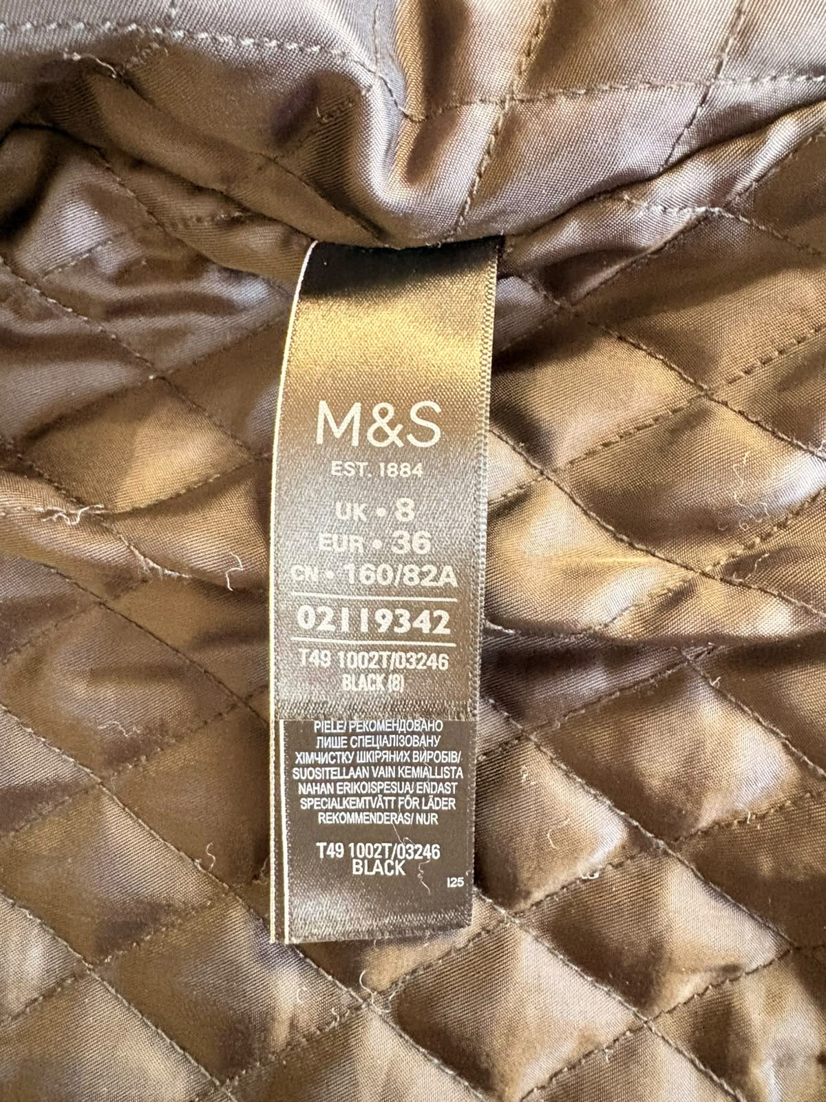 Close-up of an M&S quilted garment label sewn onto a black diamond-quilted fabric background.