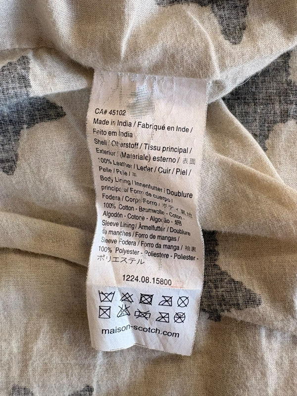 Close-up of a garment's interior care label reading 'maison scotch' and product details, attached to light beige and gray patterned fabric.