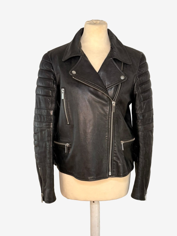 A black leather motorcycle jacket with silver zippers and quilted sleeve panels, displayed on a beige mannequin torso against a light gray background.
