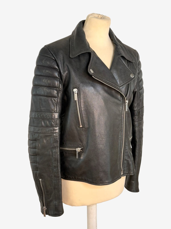 A black leather motorcycle jacket with silver zippers, displayed on a beige mannequin torso against a plain white background.